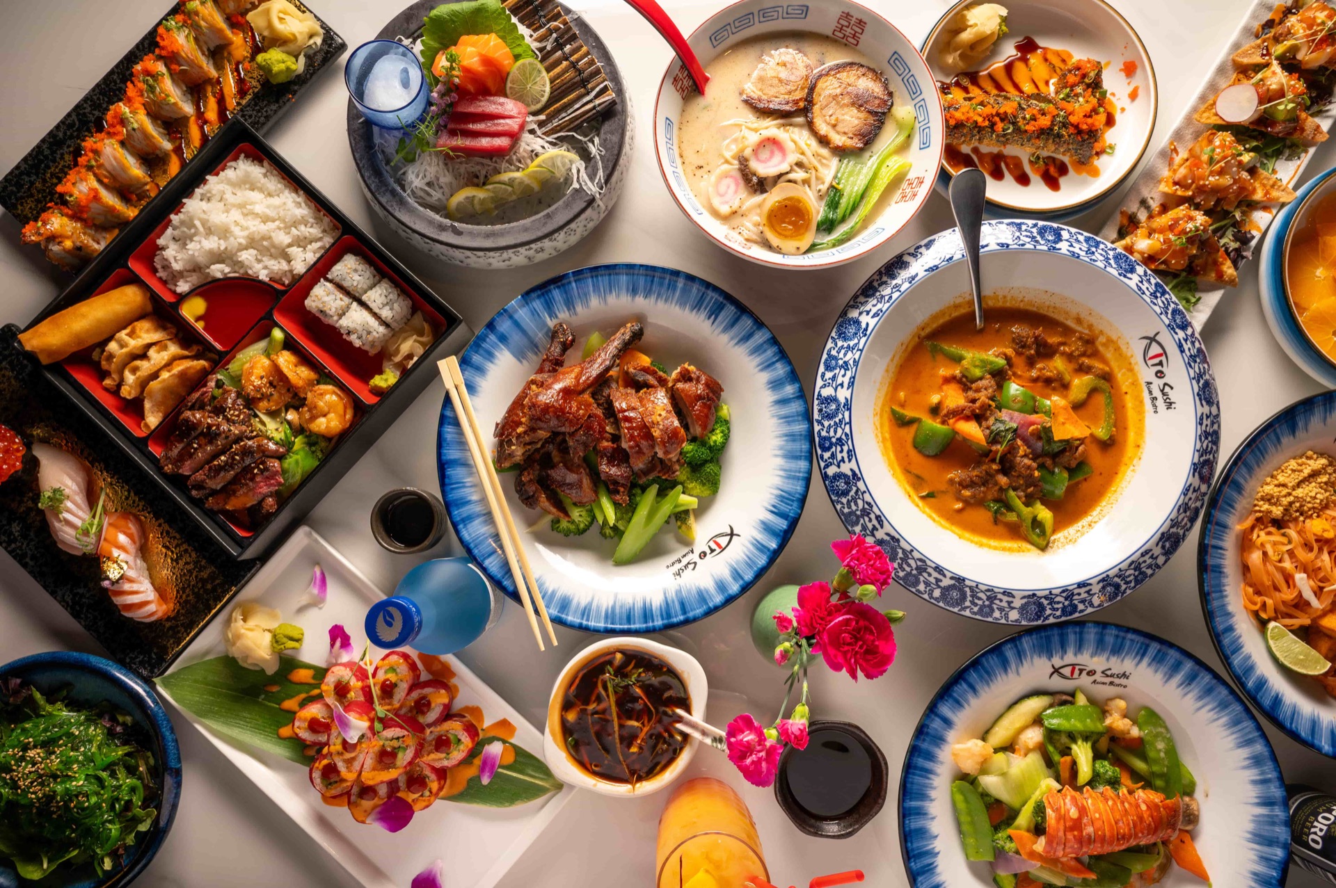 Full table of East Moon Asian Bistro dishes - sushi rolls, ramen, Thai curry, roast duck and bento box in Centennial CO