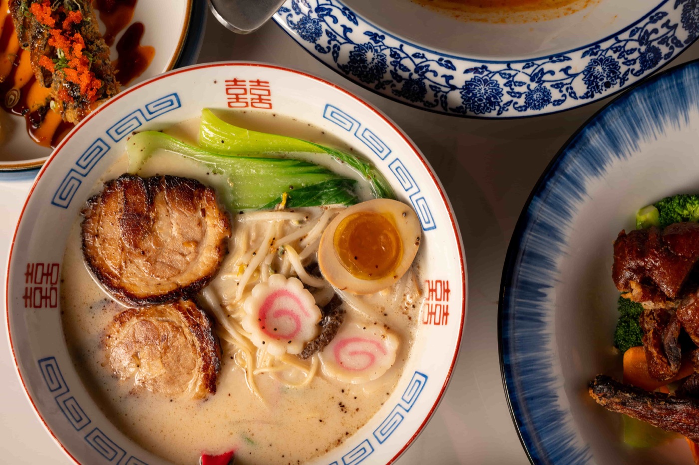 Overhead view of ramen, roast duck and Thai curry on a shared table at East Moon Asian Bistro Centennial CO